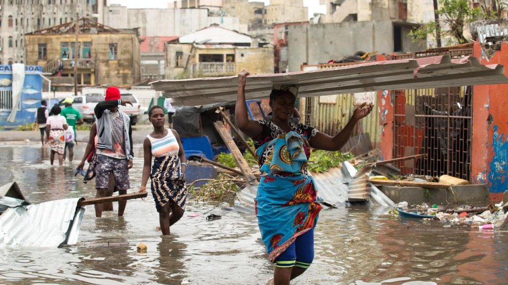 Cyclone Idai, Mozambique, aftermath. Women wading through flood waters on a city street, carrying large loads of salvaged corrugated metal sheets. 